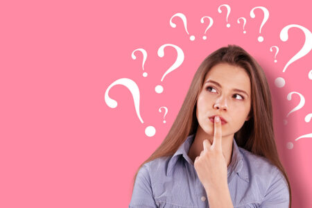 Frau vor rosa Wand mit Fragezeichen denkt nach | Neugierige Fragen von Interessenten beim Immobilienverkauf
