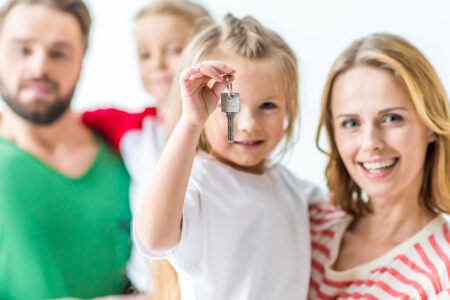 Eine Familie vor einem weißen Hintergrund lächelt, ein Mädchen hält einen Schlüssel in der Hand - Immobilienkauf