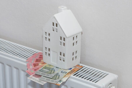 Ein weißes Minihaus auf einer Heizung mit Geldscheinen - Betriebskosten